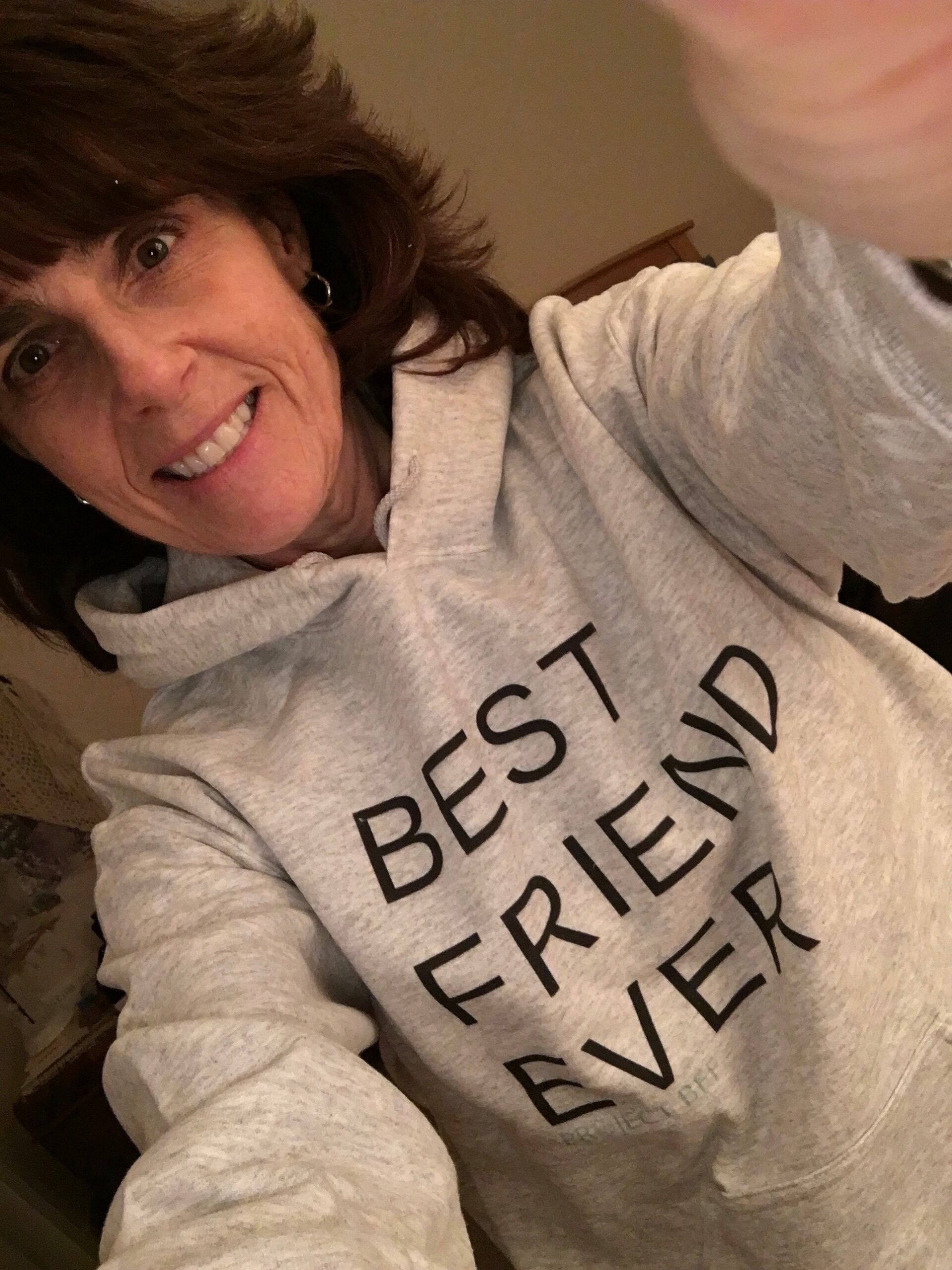 Photo of Terri, smiling brown-haired woman wearing a gray hooded sweatshirt with the words "Best friend forever."